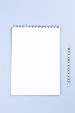 Boş beyaz sayfa ve açık gri masa arkaplanlı kalem içeren spiral bir defter aç. Dikey üst görünüm, metin için boşluk kopyala