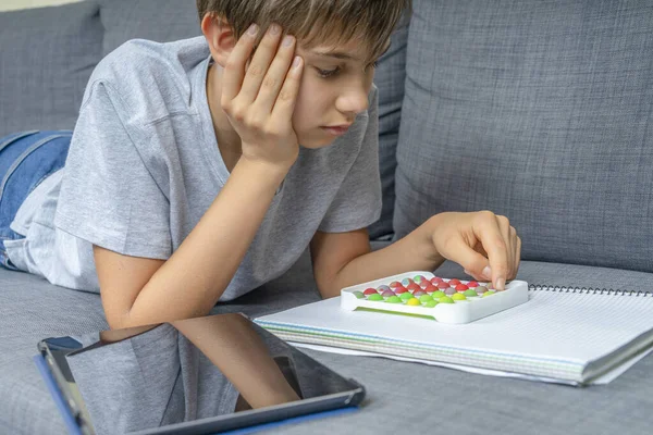 Menino adolescente deitado no sofá e brincando com pop sensorial brinquedo inquieto depois de aprender com o computador tablet digital, fazendo lição de casa em casa — Fotografia de Stock