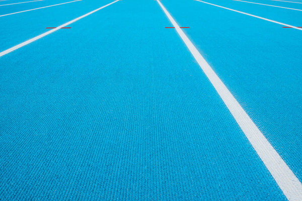 Спортивный фон. Голубая беговая дорожка с белыми линиями и красной меткой на спортивном стадионе. Вид сверху
