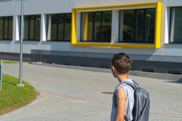 Εφηβικό αγόρι σε προστατευτική μάσκα με αυτοκόλλητο γύψο επίδεσμο στο χέρι του χαρούμενος πίσω στο σχολείο μετά τις καλοκαιρινές διακοπές — Φωτογραφία Αρχείου