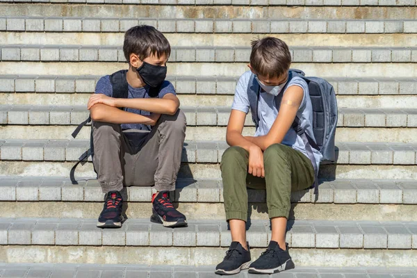 팔에 부착성 반창고가 있는 방독면을 쓰고 있는 10 대 소년은 친구와 백신 접종에 관해 이야기한다. 밖에서 계단에 앉아 있는 어린이들 — 스톡 사진
