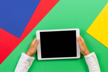 Çocuk elleri açık yeşil, mavi, kırmızı zemin üzerinde beyaz dijital tablet bilgisayarı tutuyor. Üst görünüm