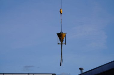 Vinç inşaat alanında çimento dolu koni şeklindeki bir tankı hareket ettiriyor.