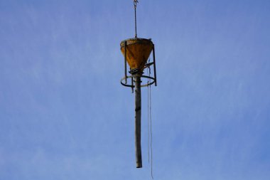 Vinç inşaat alanında çimento dolu koni şeklindeki bir tankı hareket ettiriyor.