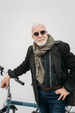 Beyaz bir duvarın yanında bisikletle duran yaşlı, gri saçlı hippi görünümlü bir iş adamı. İşe git, mola ver. Yaşlılar yaşam konsepti.