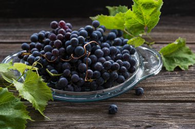 Eski ahşap bir masada, cam bir tabakta olgun üzümler.