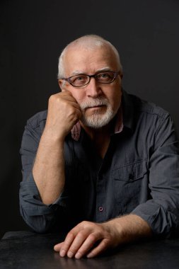 Yetişkin, gri saçlı, gözlüklü bir adam kameraya bakar, başını elinin üzerine koyar. Portre, stüdyo, yakın çekim, yüze odaklan..