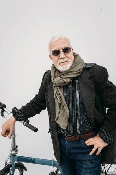 Beyaz bir duvarın yanında bisikletle duran yaşlı, gri saçlı hippi görünümlü bir iş adamı. İşe git, mola ver. Yaşlılar yaşam konsepti.