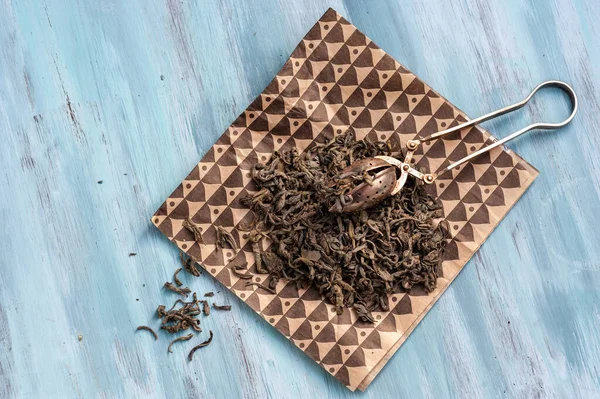 dry green tea leaves with tea strainer on a blue background, top view