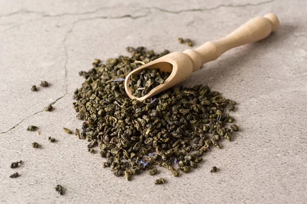 dry green tea leaves of the highest grade with a wooden measuring spoon on a light background, top view