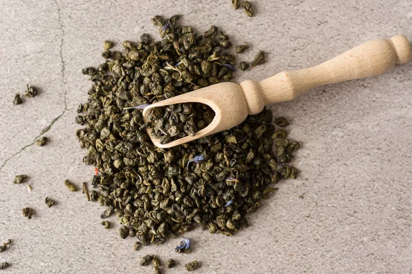 dry green tea leaves of the highest grade with a wooden measuring spoon on a light background, top view