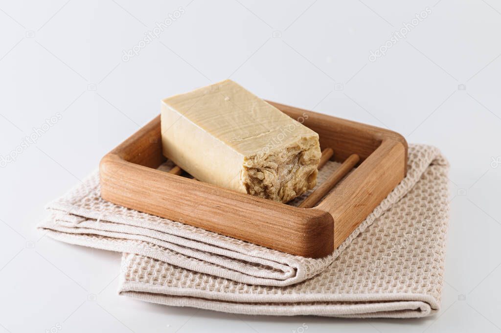 natural handmade soap on a wooden soap dish, side view, on a bath towel, light background