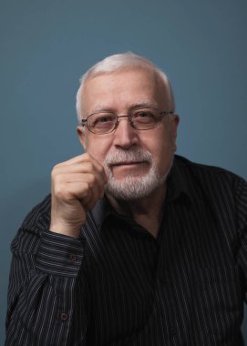 Yaşlı, yakışıklı, karizmatik bir adam kameraya, stüdyoya, karanlık arkaplana, portreye bakıyor.