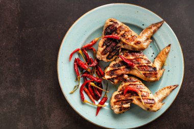 Izgara tavuk kanadı, büyük bir tabakta, üst manzara, kahverengi arka plan.