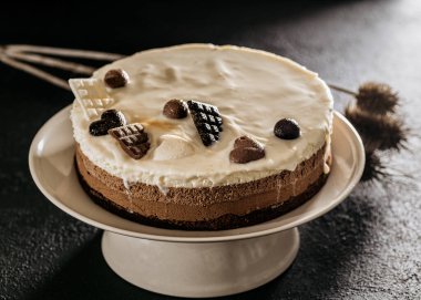 Doğum günü pastası üç çikolata, çikolata kalpler ve külçeler bir tabakta, gri arka planda servis edildiğinde kurumuş çiçeklerle süslenmiş.