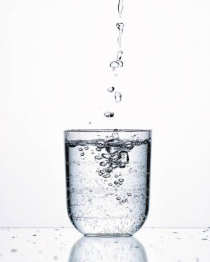 Bir bardağa maden suyu dök, beyaz bir zemin üzerine, su sıçratır ve ağlar.