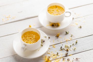 İki fincan aromatik çiçek çayı, yatıştırıcı, alternatif ilaç, beyaz ahşap arka planda tıbbi malzeme.