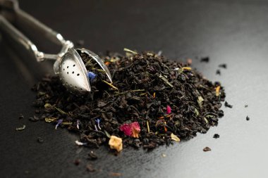 Koyu arkaplanda meyveli kuru çay ve süzgeç karışımı.