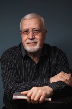 Yaşlı, yakışıklı, karizmatik bir adam. Gözlüklü, gülümseyen, stüdyo, karanlık arka plan, portre.