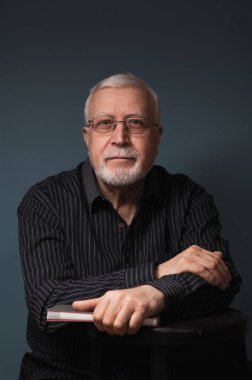 Yaşlı, yakışıklı, karizmatik bir adam. Gözlüklü, not defteri, stüdyo, koyu arkaplan, portre.