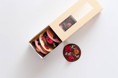 Meyve ve fındıklı doğal malzemelerden elde üretilen sağlıklı çok renkli çikolatalar beyaz arka planda bir hediye kutusuna konur.