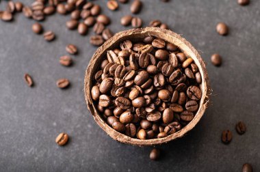 Siyah kahve çekirdekleri, hindistan cevizi kasesinde aromatik, masaya serpiştirilmiş fasulye.