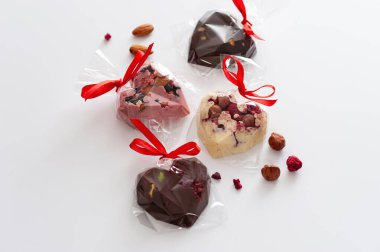 Çilekli, böğürtlenli, böğürtlenli ve bademli, pembe, süt ve beyaz çikolatalı kalpler şeklinde karıştırılmış çikolatalar, bir kurdele, el yapımı, üst görünüm, beyaz bir arka planda.