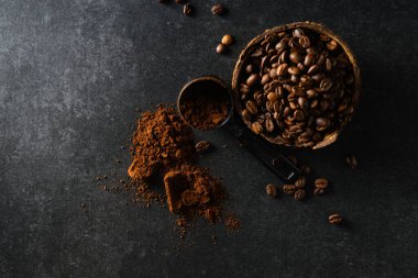 Hindistan cevizi kasesindeki kahve çekirdekleri masaya saçılmış koyu gri arka plan, mesaj için boş alan.