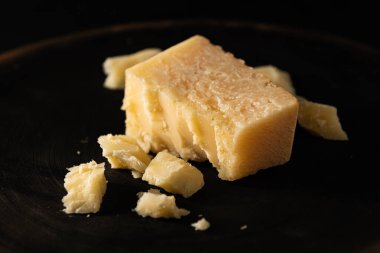 Dilimlenmiş parmesan peyniri, parçalanmış, koyu arkaplanda.