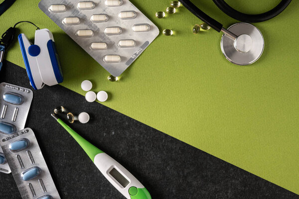 pulse oximeter, blood oxygen meter, electronic thermometer, tonometer, tablets on a gray-green background, top view, empty space for text