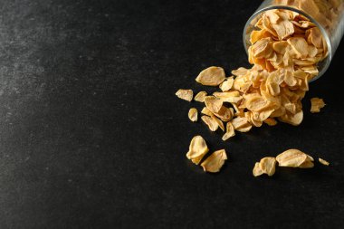 Koyu gri arka planda cam bir kasede kuru doğranmış sarımsak dilimleri, üst manzara, metin için boş alan