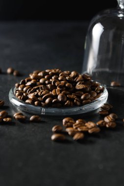 Kahve çekirdekleri gri bir arka planda cam bir tabağın üzerinde, yakın plan.