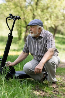 Olumlu, yaşlı bir adam parkta yürüyüşe çıktı, durdu ve elektrikli bir scooter 'ın yanına oturdu. Yaz, güneşli bir gün. Yaşlıların sağlıklı yaşam tarzı.