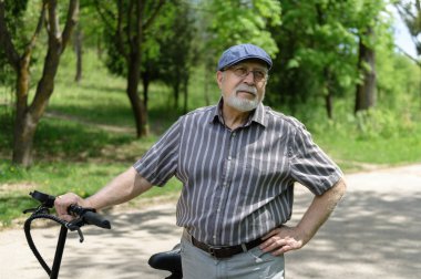 Olumlu, karizmatik yaşlı bir adam eko scooterla parkta yürüyüşe çıktı. Yaşlıların sağlıklı yaşam tarzı.