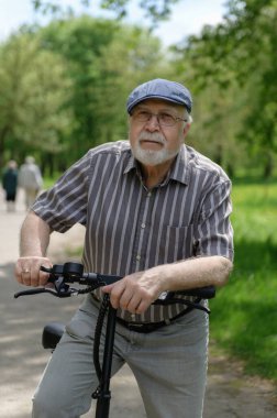 Olumlu, karizmatik yaşlı bir adam eko scooterla parkta yürüyüşe çıktı. Yaşlıların sağlıklı yaşam tarzı.