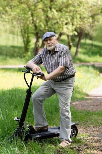 Olumlu, yaşlı bir adam parkta yürüyüşe çıktı, durdu ve yanında elektrikli bir scooter duruyordu. Yaz, güneşli bir gün. Yaşlıların sağlıklı yaşam tarzı.
