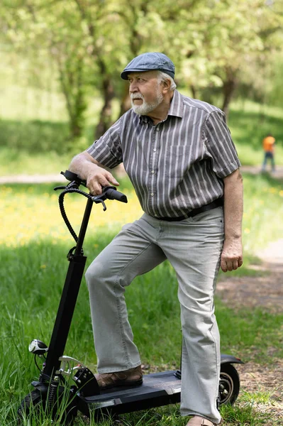 Olumlu, yaşlı bir adam parkta yürüyüşe çıktı, durdu ve yanında elektrikli bir scooter duruyordu. Yaz, güneşli bir gün. Yaşlıların sağlıklı yaşam tarzı.