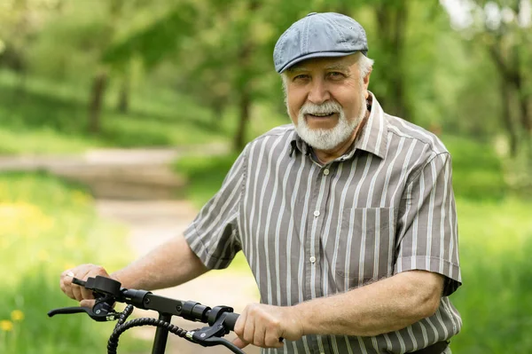 Olumlu, yaşlı bir adam parkta yürüyüşe çıktı, durdu ve yanında elektrikli bir scooter duruyordu. Yaz, güneşli bir gün. Yaşlıların sağlıklı yaşam tarzı.