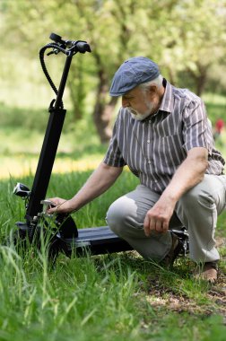 Olumlu, yaşlı bir adam parkta yürüyüşe çıktı, durdu ve elektrikli bir scooter 'ın yanına oturdu. Yaz, güneşli bir gün. Yaşlıların sağlıklı yaşam tarzı.