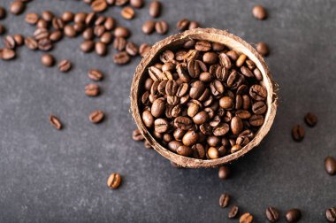 Siyah kahve çekirdekleri, hindistan cevizi kasesinde aromatik, masaya serpiştirilmiş fasulye.