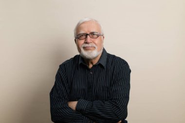 Gözlüklü ve siyah gömlekli yaşlı adam kollarını göğsüne bağladı ve sırıtarak, bel portresi, açık arkaplan, stüdyo