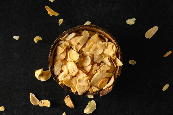 Hindistan cevizi kasesinde kurumuş sarımsak taneleri, yukarıdan koyu gri arka planda düşen taneler, üst manzara.