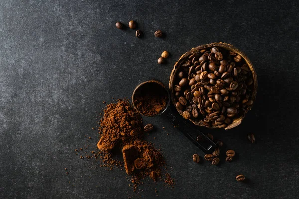 Hindistan cevizi kasesindeki kahve çekirdekleri masaya saçılmış koyu gri arka plan, mesaj için boş alan.