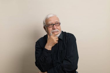 Yaşlı, gri saçlı, gözlüklü ve siyah gömlekli bir adam. El sakallı, çerçevede duyguları olan, bel portresi, açık arkaplan, stüdyo.