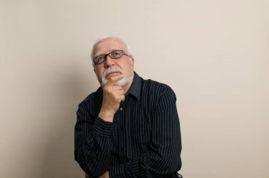 Yaşlı, gri saçlı, gözlüklü ve siyah gömlekli bir adam. El sakallı, çerçevede duyguları olan, bel portresi, açık arkaplan, stüdyo.