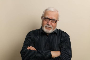 Gözlüklü ve siyah gömlekli yaşlı adam ellerini göğsüne, beline, beline, arka planına, stüdyosuna koydu.