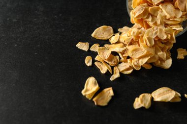 Koyu gri arka planda cam bir kasede kuru doğranmış sarımsak dilimleri, üst manzara, metin için boş alan