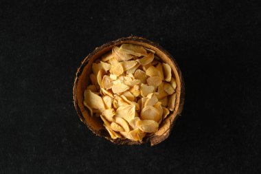 dry flakes of garlic in a coconut bowl, on a dark gray background, top view