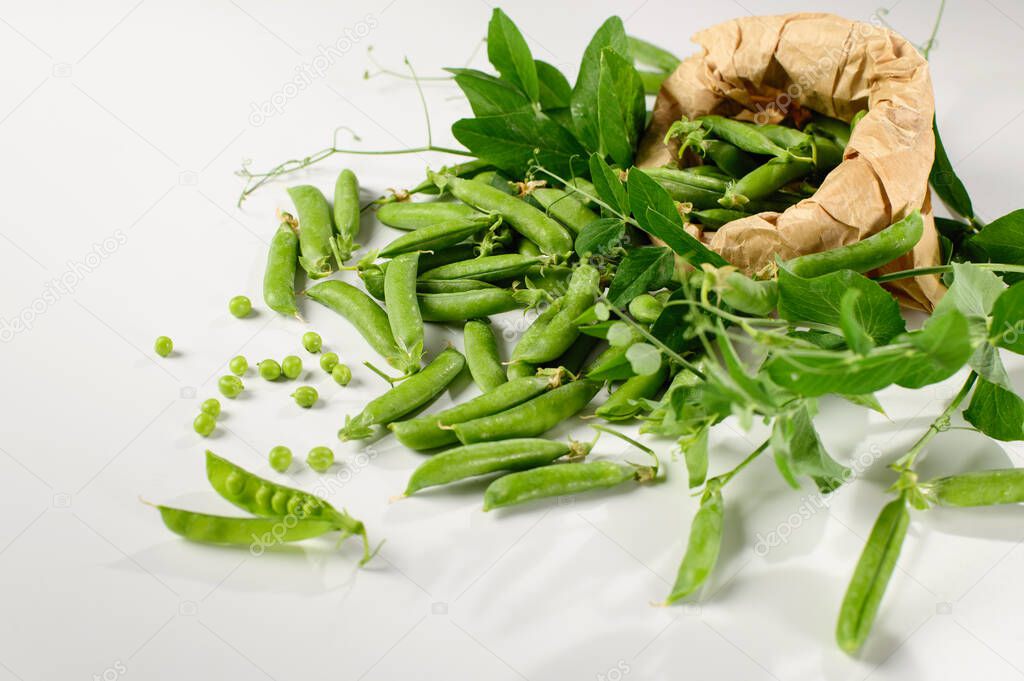 green young peas in pods, in a craft bag, freshly picked on a white background, top-side view, close-up