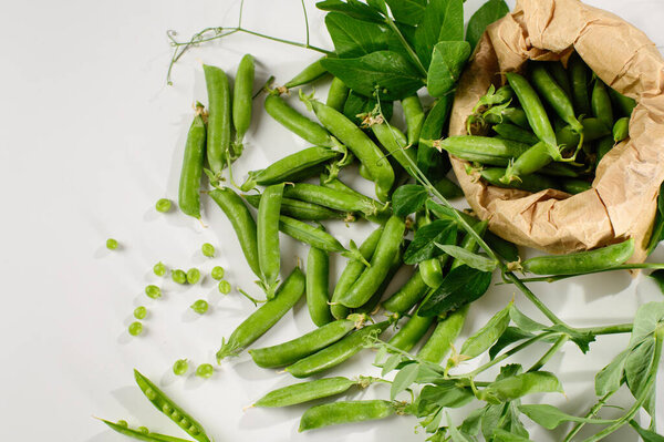 green young peas in pods, in a craft bag, freshly picked on a white background, top view, close-up